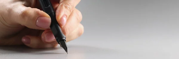 Close-up of person holding black feather pen, sharp tip, tool for writing. Pen on grey surface. Stationery, writing, office supplies concept. Copy space