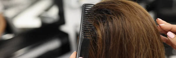 Close-up of professional hairdresser brushing clients hair with comb, shiny hairstyle. Female client sit in masters chair. Wellness, beauty salon concept