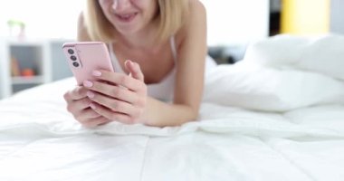 Gülümseyen kadın yatakta yatarken akıllı telefonuyla mesaj atıyor. Sosyal ağlar konseptinde iletişim
