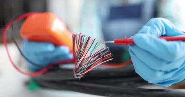 Usta tamirci test cihazıyla kablodan çıkan çok renkli kabloları test ediyor. Elektrik voltajı konsepti denetleniyor