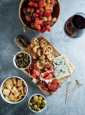 Geleneksel İspanyol ya da İtalyan mezeleri. Jamon iberico, mavi peynir, kraker, zeytin, üzüm ve kuru kırmızı şarap, gri taş arka plan. Üst görünüm