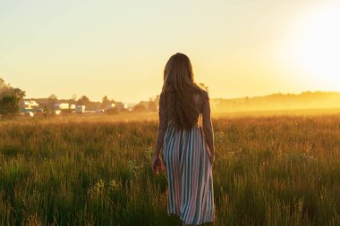 Yeşil bir tarlada giyinmiş bir kız batan güneşin parlak ışınlarında