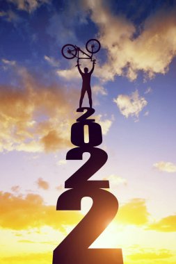 Gün batımında 2022 sayısının üzerinde bisikleti olan bir bisikletçinin silueti. Yeni yıl konsepti. 