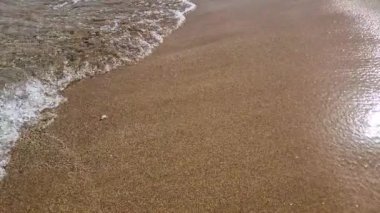 Kumsalda küçük deniz dalgaları yavaş hareket ediyor.