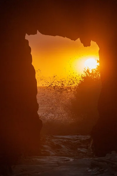 The setting sun is peaking through the keyhole arch at Pfeiffer Beach, near Big Sur.