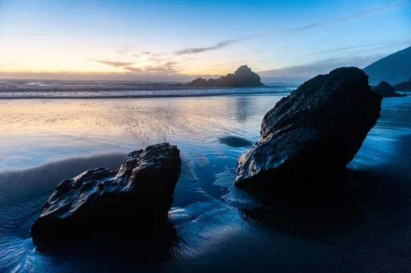 Gün batımında Pfeiffer sahilindeki kayalıklarda. Koyu sarı turuncu bulutlar gökyüzünü renklendirir.