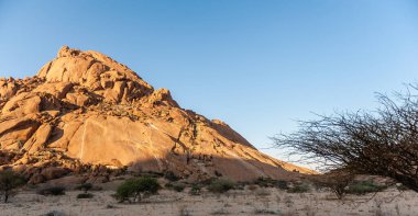Batan güneşin son ışınlarında parlak turuncu renkte parlayan kalın kaya oluşumları. Spitzkoppe, Namibya.