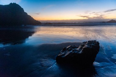 Gün batımında Pfeiffer sahilindeki kayalıklarda. Koyu sarı turuncu bulutlar gökyüzünü renklendirir.