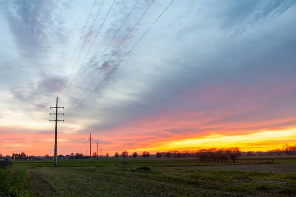 The setting sun in the flemish country side colors the sky intensely yellow and orange.