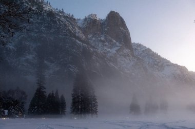 Ürkütücü bir sis Yosemite Vadisi 'nin zeminini kaplarken ince bir kar tabakası güzel bir günbatımında ağaçları çevreleyecek..