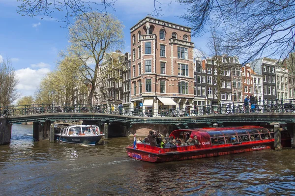 Ámsterdam, Países Bajos 14 de abril de 2012. Buque de placer navega a través del canal en el centro de la ciudad más allá de las antiguas casas de arquitectura tradicional — Foto de Stock
