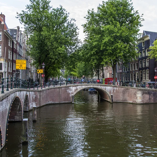 Amsterdam, Nederland, op 7 juli 2014. typisch stedelijke weergave met huizen aan de oever van het kanaal en de oude stenen brug — Stockfoto