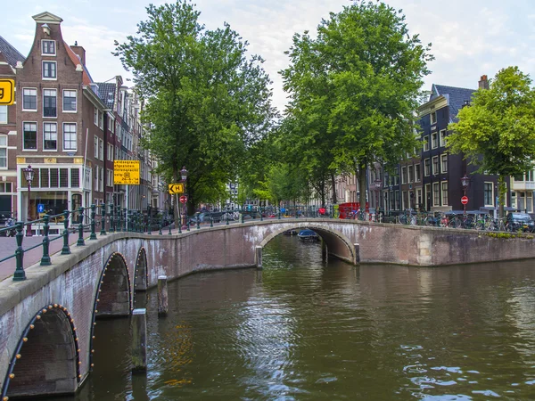 Amsterdam, Nederland, op 7 juli 2014. typisch stedelijke weergave met huizen aan de oever van het kanaal en de oude stenen brug — Stockfoto