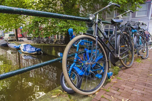 Amsterdam, Netherlands, on July 10, 2014. Bicycles are parked on the city street on the bank of the channel — Stock Photo, Image