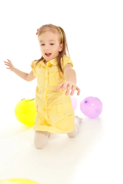 Lustiges kleines Mädchen, das auf dem Boden sitzt und mit Luftballons spielt — Stockfoto
