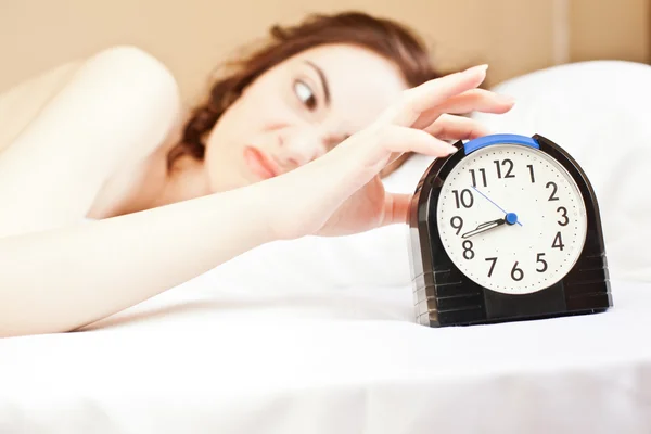 Woman lying a bed and holding an alarm (focus on woman) — Stock Photo, Image