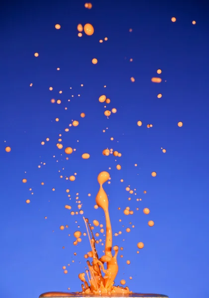 Spritzer bunte Flüssigkeit auf blauem Hintergrund — Stockfoto