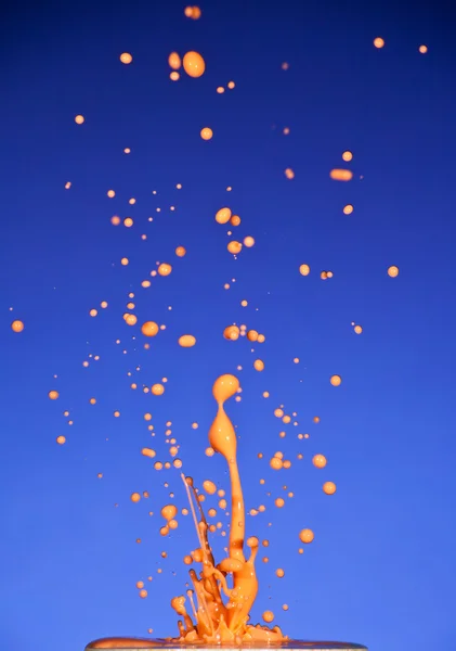 Spritzer bunte Flüssigkeit auf blauem Hintergrund — Stockfoto