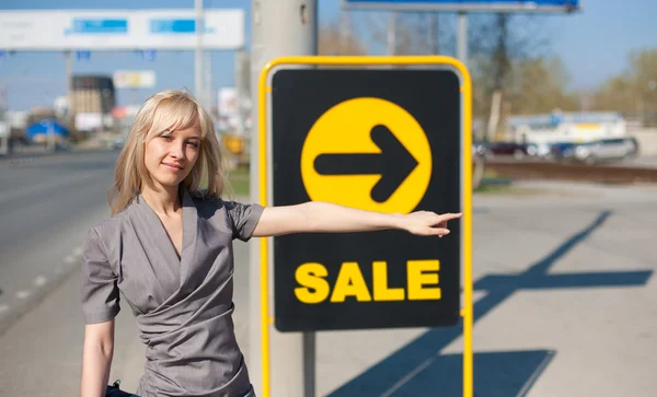 Kobieta stojąc na zewnątrz w pobliżu transparent z napisem Sprzedam — Zdjęcie stockowe