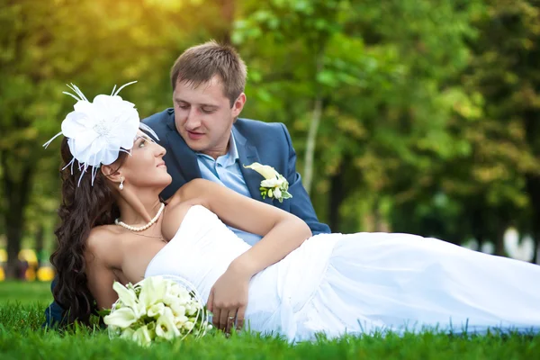 Счастливые невеста и жених лежат на зеленой траве — стоковое фото