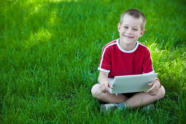 Pojken sitter med en laptop på gräset — Stockfoto