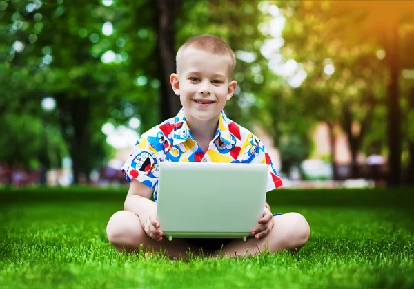 Netter kleiner Junge sitzt mit Laptop im Gras — Stockfoto