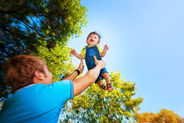 Happy daddy is throwing baby in a greenl summer park