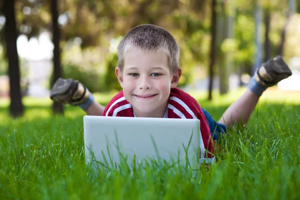 Sechsjähriger Junge liegt mit Laptop im Park — Stockfoto