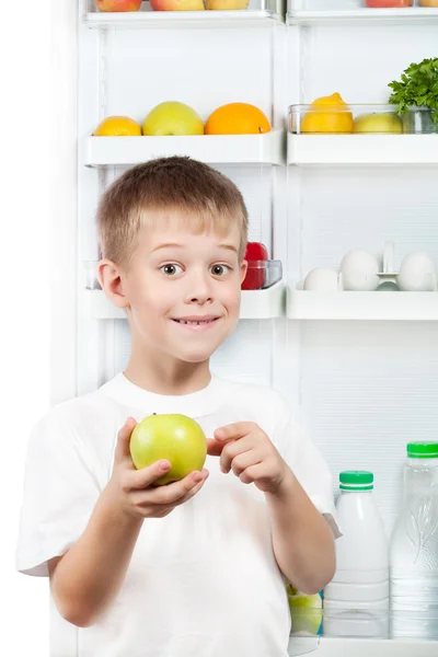 Cute boy is holding an apple near the open refrigerator — Stock Photo, Image