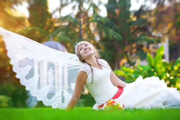 Szczęśliwa panna młoda w białej sukience leży na zielonej trawie — Zdjęcie stockowe