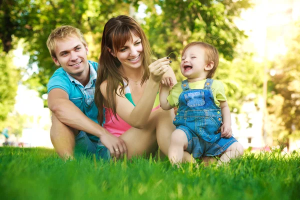 Happy family on a green lawn in park — Stock Photo, Image
