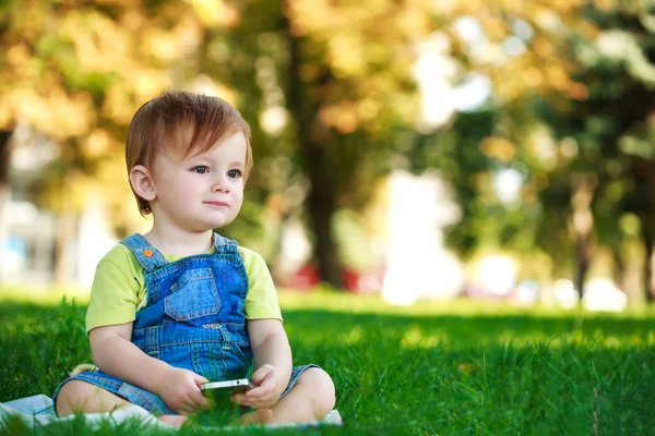 Söt baby spelar med telefon på det gröna gräset — Stockfoto