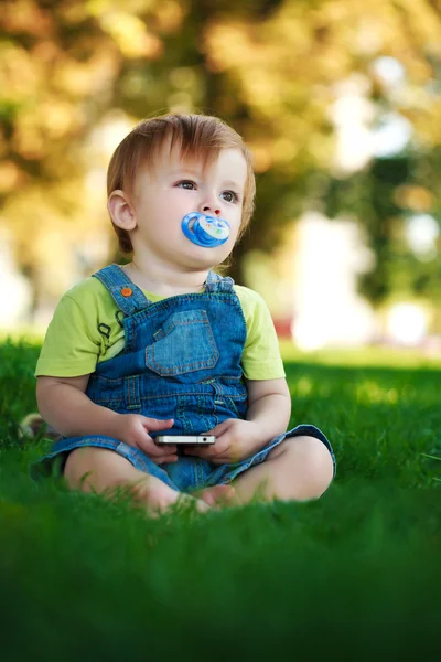 Barnet leker med telefonen i parken — Stockfoto