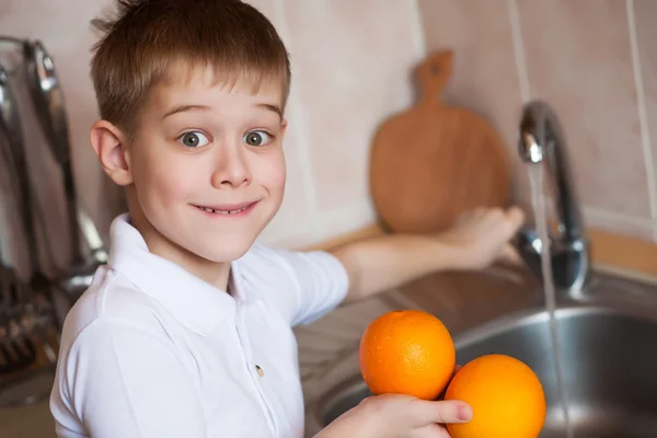 Маленький хлопчик миє фрукти на кухні — стокове фото