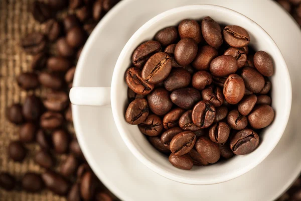 Granos de café tostados en una taza en arpillera —  Fotos de Stock