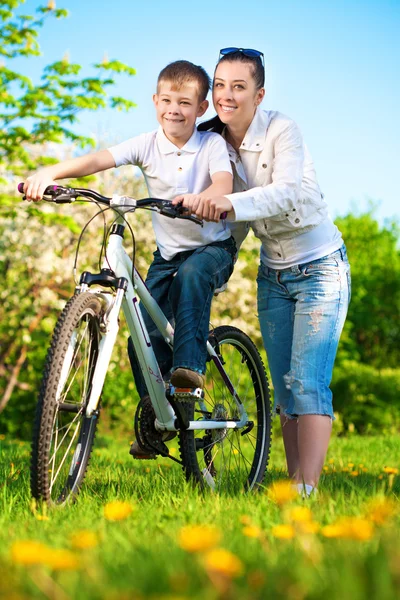 Família em um parque verde com uma bicicleta — Fotografia de Stock