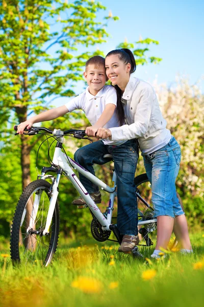 Gelukkig moeder en zoon in een groen park met een fiets — Stockfoto
