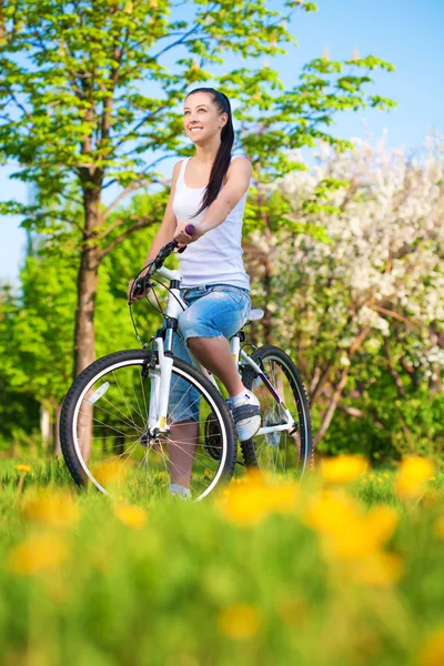 Cute woman in a green park on a bike — Stock Photo, Image