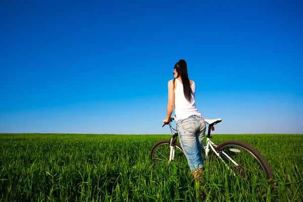 一辆自行车上的绿色字段中的女人 — 图库照片