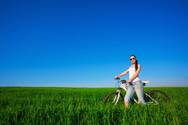 Woman in a green field on a bike — Stok fotoğraf