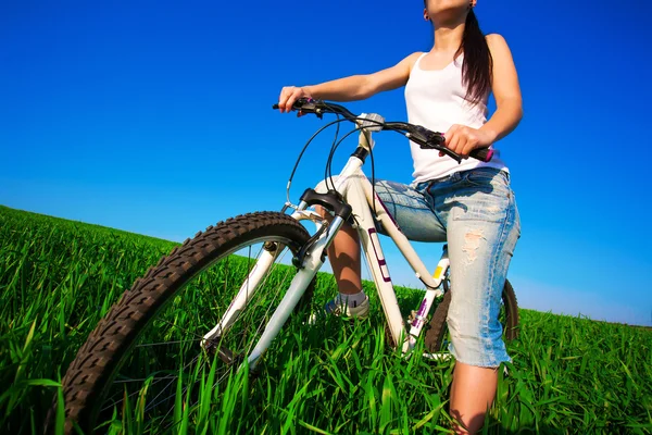 Brunette vrouw in een groene veld op een fiets — Stockfoto