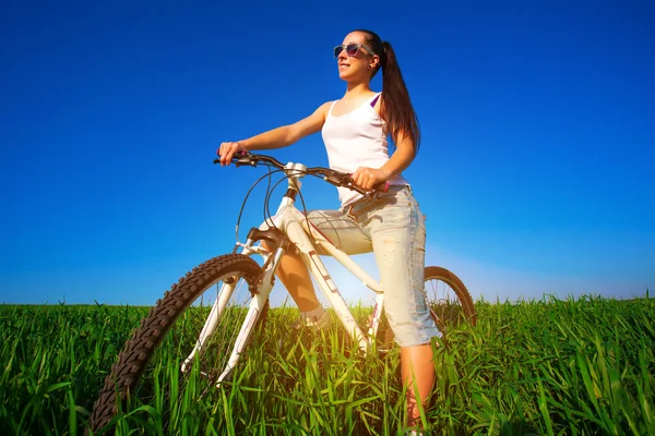 Woman in a green field on a bike — Stockfoto