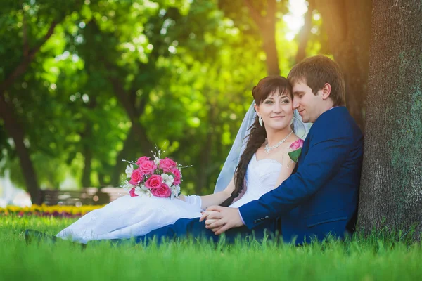 Happy newlyweds are sitting on the green grass — Stock Photo, Image