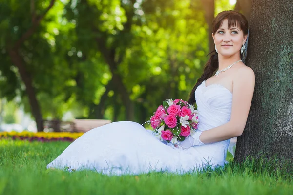 Bruden i vit klänning sitter under ett träd — Stockfoto