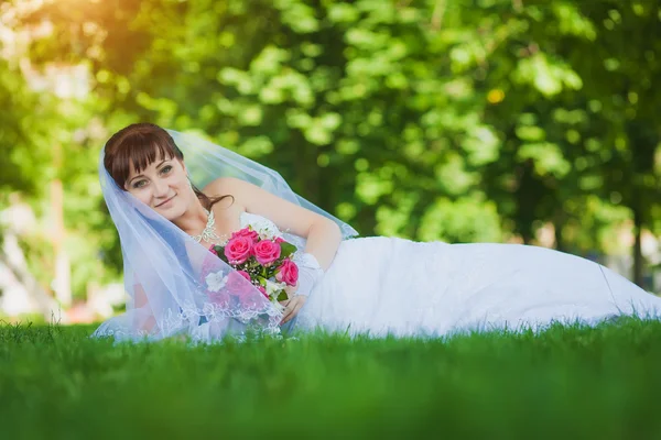 Lyckliga bruden i vit klänning liggande på grönt gräs — Stockfoto