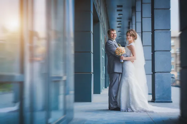 Новобрачные обнимаются с голубым современным зданием — стоковое фото