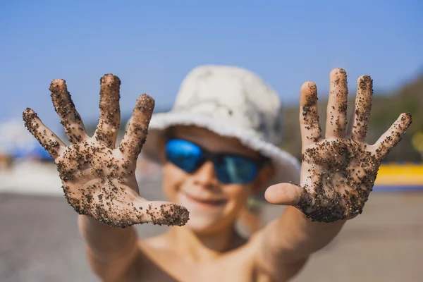 Menino feliz na praia está brincando com seixos — Fotografia de Stock