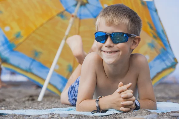 Feliz niño sonriente está tomando el sol en una playa —  Fotos de Stock