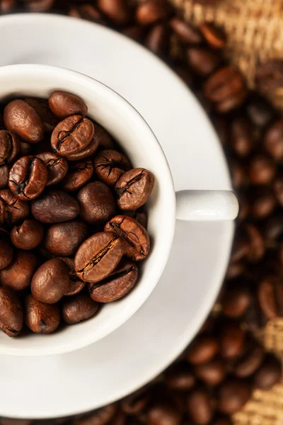 Granos de café asados en una taza sobre fondo de arpillera —  Fotos de Stock