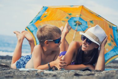 Anne ve oğlu bir kumsalda güneş banyosu